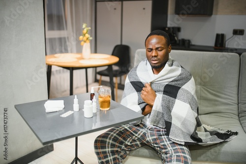 Shot of a young man with a cold recuperating at home. Feeling bad. Sick African-American man covered with white duvet drinking hot healing tea in bed photo