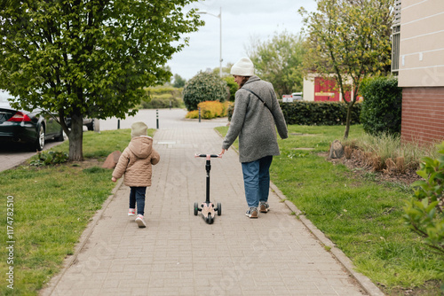 Mother supports her daughter while she learns to ride a scooter outdoors, close-up. The concept of solo parenting and raising children.