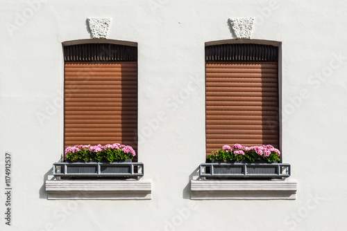 House with white walls and a pair of windows and colorful flowers in Germany. Sunlight and shadow. Details of typical German architecture.