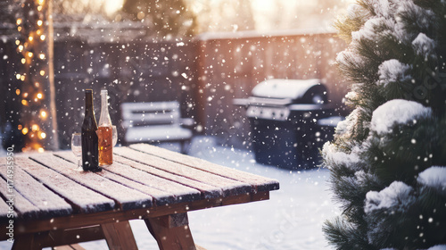 cozy winter backyard scene featuring wooden table with bottles, surrounded by falling snowflakes. grill is visible in background, creating warm atmosphere for gatherings