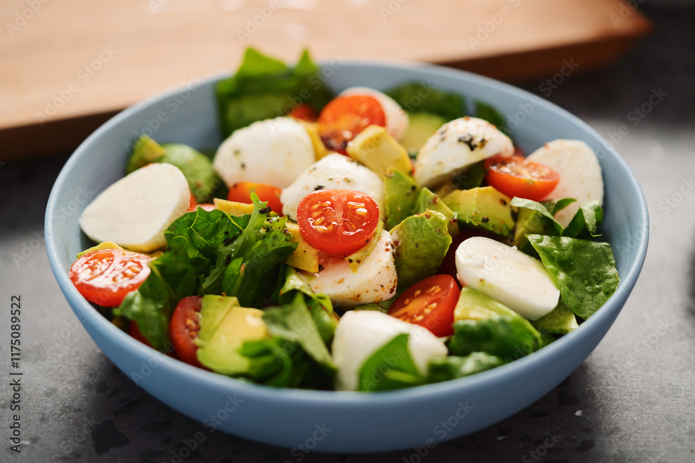 Salad with avocado, cherry tomatoes, romaine and mozzarella in blue bowl on concrete countertop Salad with avocado, cherry tomatoes, romaine and mozzarella in blue bowl on concrete countertop