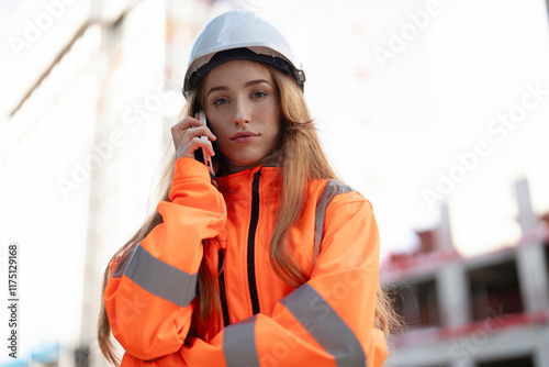 Coolheaded calm ravishing young female Construction worker in safety gear communicates on phone at building site during daylight hours