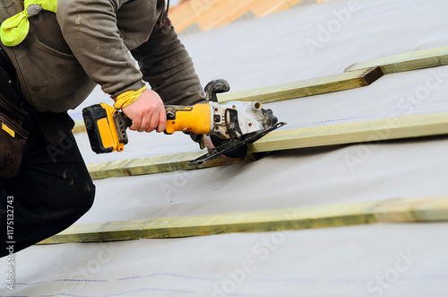 Construction worker roofer using power tool to cut wood on a roof during daylight hours photo