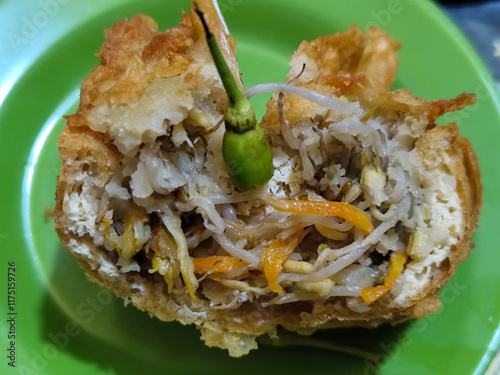 Tahu Isi or Tahu Brontak is an Indonesian food made from fried tofu with several types of vegetables including cabbage, mustard greens, bean sprouts and carrots. Served with chili on a green plate. photo