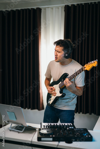 Asian male producer layering vocals over electronic beats, guitar and audio gear on the desk, in a modern and inspiring studio environment. photo