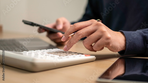Obraz na płótnie A close-up of a person's hands working with a calculator, smartphone, and laptop on a desk. financial management, budgeting, and productivity in a professional workspace. w salonie