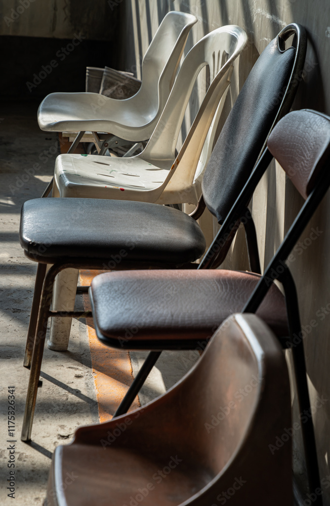 Perspective side view of Different of Chairs with Morning sunlight shines through with concrete wall in the background. use it as your Wallpaper, Poster and Copy space, Selective focus.