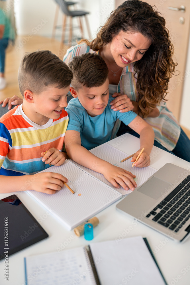 Caucasian mother in casual attire assists two elementary-aged boys with schoolwork using laptop and notebooks at home dining table. Caucasian mother in casual attire assists two elementary-aged boys with schoolwork using laptop and notebooks at home dining table.