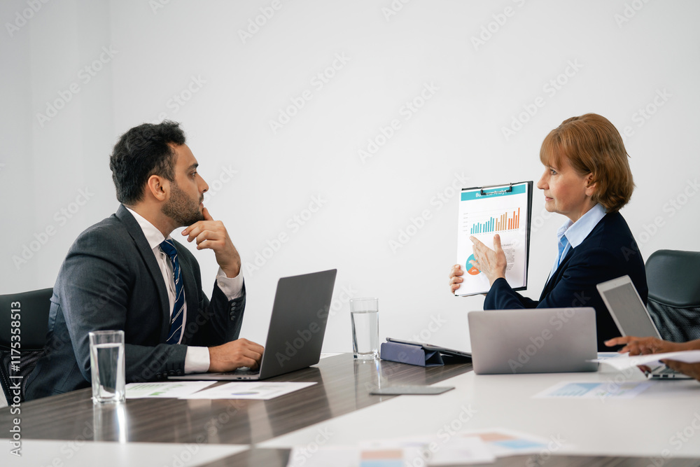 Two people in suits are sitting at a table with a presentation in front of them Two people in suits are sitting at a table with a presentation in front of them