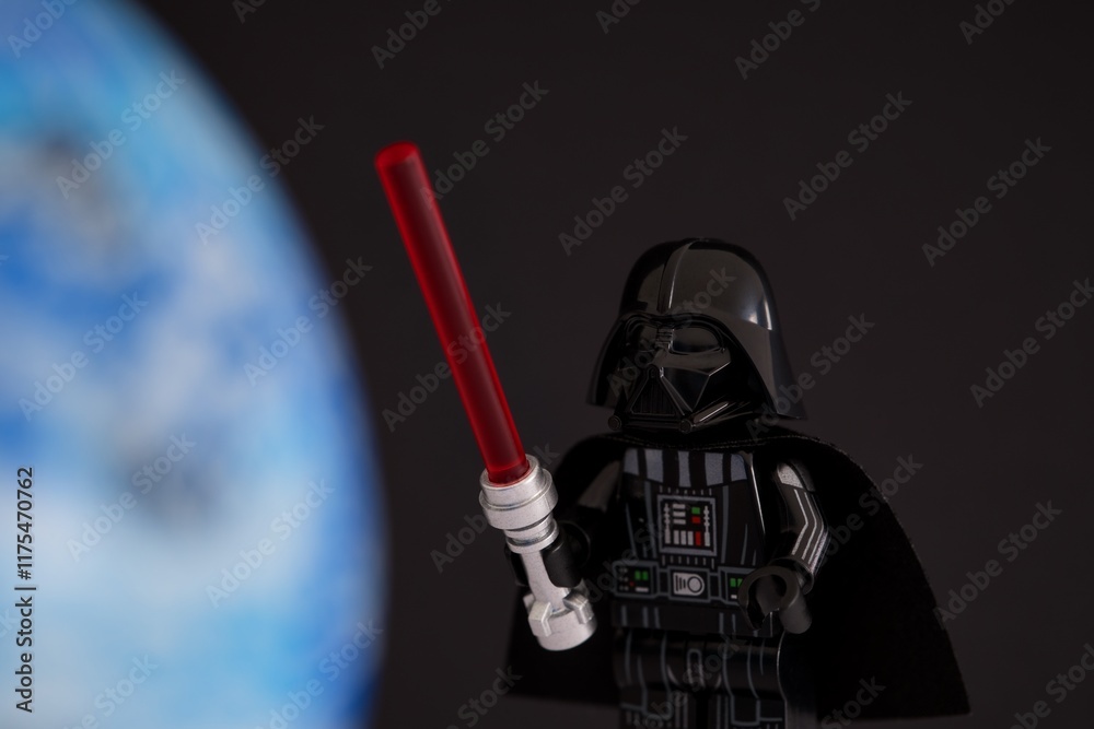 Fototapeta premium Tambov, Russian Federation - November 14, 2024 Lego Darth Vader minifigure with red lightsaber against a black background with blue planet