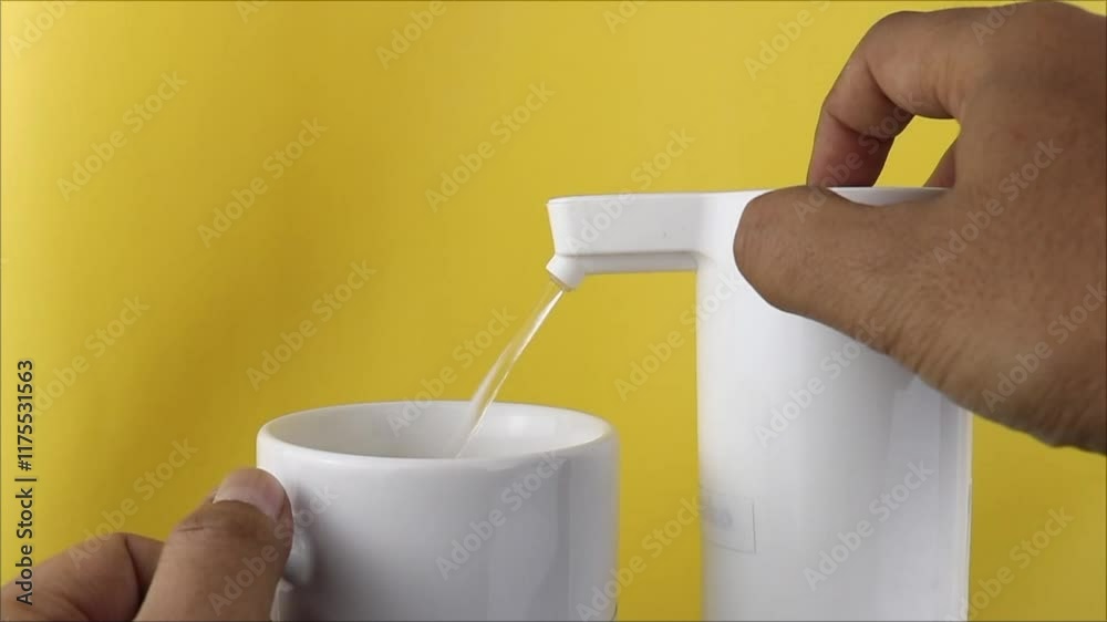 Indonesian person pouring drinking water using an electric water dispenser, close-up, modern convenience, home use.