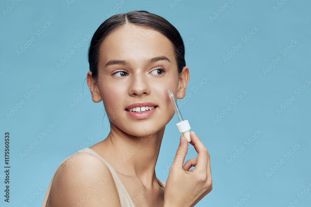 Young woman applying serum on her face, showcasing healthy skin and beauty routine with a soft expression, against a light blue background Young woman applying serum on her face, showcasing healthy skin and beauty routine with a soft expression, against a light blue background