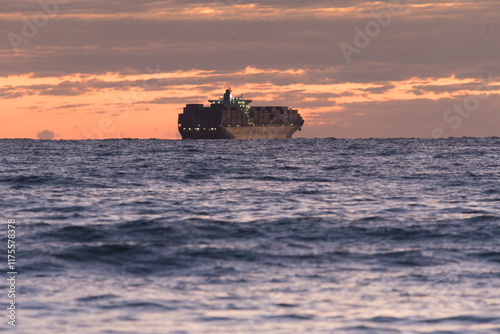 Transport ship sailing before dawn. A beautiful sunrise over the sea. Ship sailing along the sea horizon. The morning sun illuminates the sea. Sun reflections in the water sunset on the beach photo