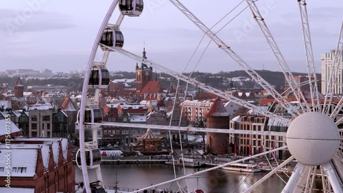 Close-Up of a Ferris Wheel with Snow-Covered Historic Old Town in the Background, Featuring Brick Architecture and Iconic Landmarks