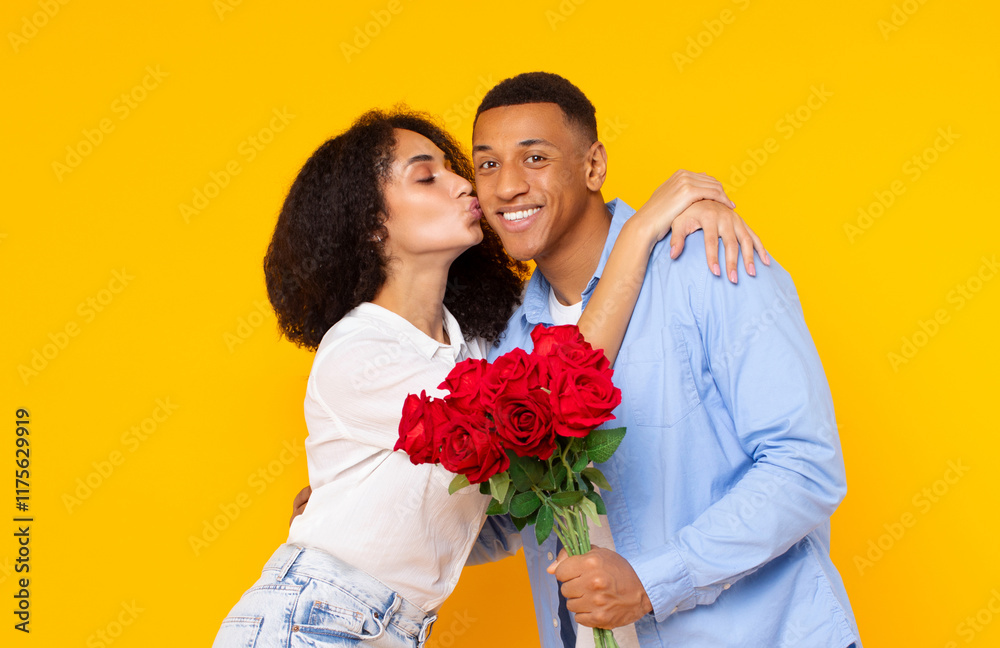 Affectionate Latin lady kissing her happy boyfriend, guy holding bouquet of roses, posing over yellow studio background. Romantic couple celebrating Valentine's Day Affectionate Latin lady kissing her happy boyfriend, guy holding bouquet of roses, posing over yellow studio background. Romantic couple celebrating Valentine's Day