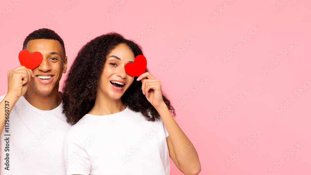 True love. Happy African American couple with red paper hearts over eyes posing together over pink background with free space, banner True love. Happy African American couple with red paper hearts over eyes posing together over pink background with free space, banner