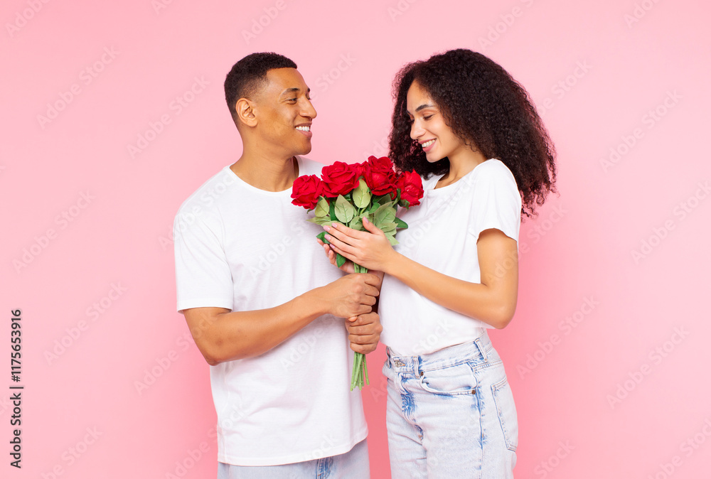 Loving African American man giving bouquet of flowers to happy lady, pampering his girlfriend with roses on Valentine's Day, pink studio background Loving African American man giving bouquet of flowers to happy lady, pampering his girlfriend with roses on Valentine's Day, pink studio background