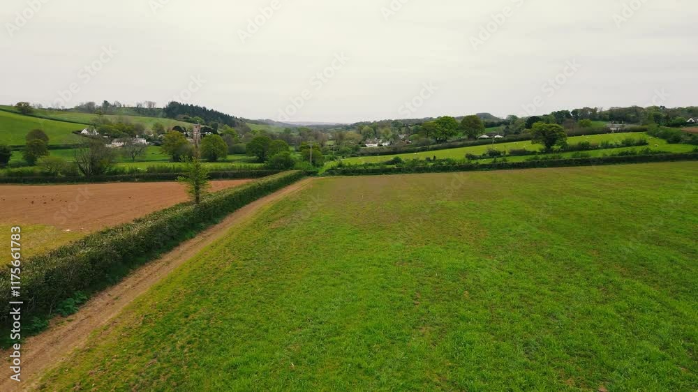 Drone view of a countryside field with lush greenery under misty sky, and a village seen in distance Drone view of a countryside field with lush greenery under misty sky, and a village seen in distance
