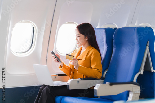 Schilderij op canvas In-Flight Online Shopping:  A young businesswoman enjoys seamless online shopping during her flight, using her smartphone and credit card while working on her laptop