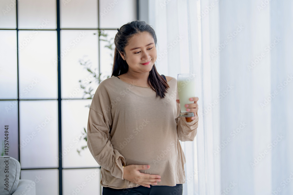 Asian female pregnant holding glass of milk in the living room, self care Asian female pregnant holding glass of milk in the living room, self care