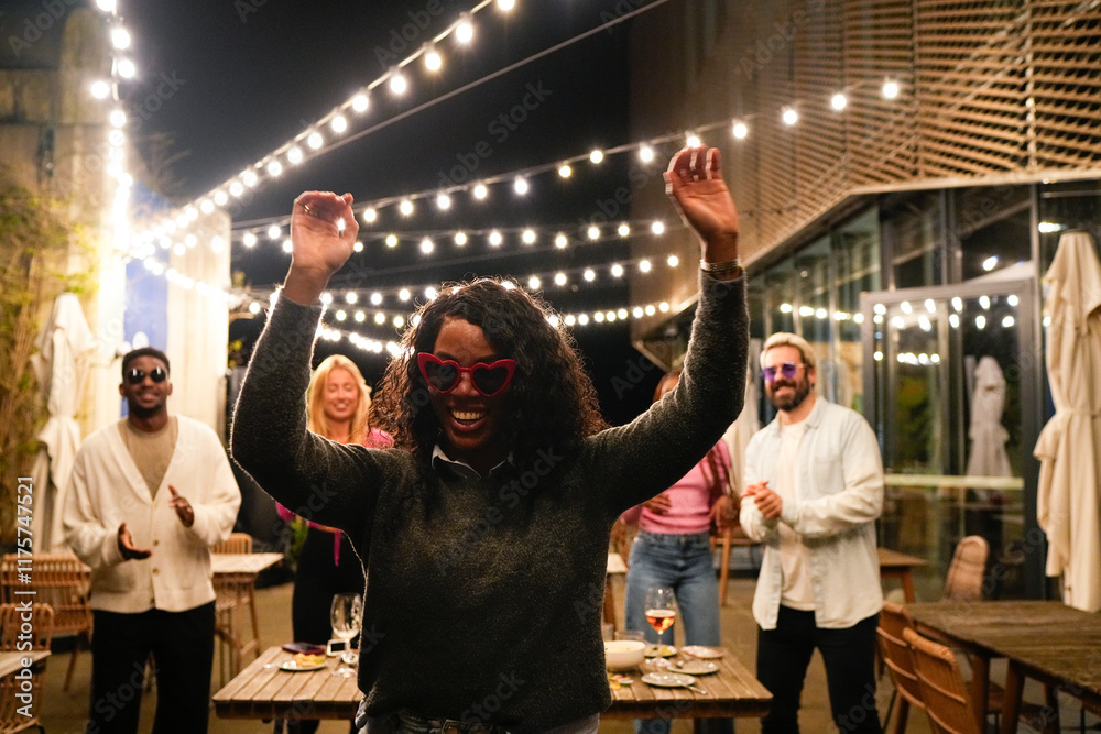 Fototapeta premium Young multiethnic friends dancing at night party under string lights