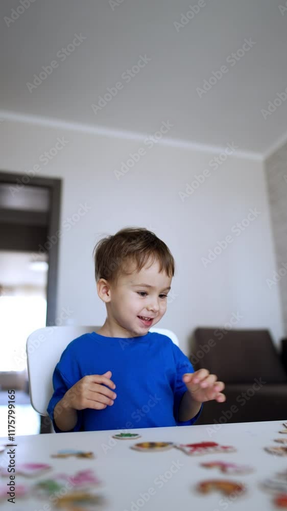 Beautiful Caucasian baby boy sitting at desk playing a game. Cheerful kid collects puzzles. Vertical video. Beautiful Caucasian baby boy sitting at desk playing a game. Cheerful kid collects puzzles. Vertical video.