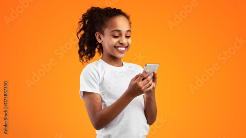 People And Technology Concept. Portrait of smiling black girl using smartphone standing isolated on yellow studio background. Happy African Americ an teen chatting online, typing sms, banner, panorama photo