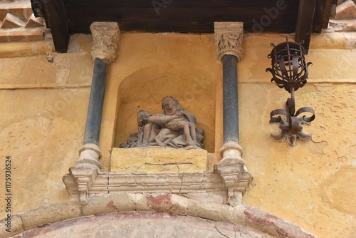 Deteriorating expressive pietà stone sculpture of distraught Virgin Mary holding lifeless body of Christ framed by dark columns at a cream colored facade in the old town of Segovia, Spain