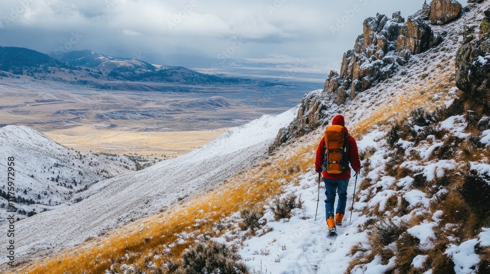 Naklejka premium Hiker ascends snowy mountain trail overlooking vast valley.