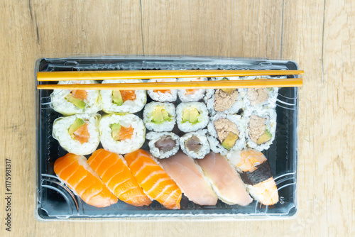 Appetizing set of nigiri sushi, uramaki and norimaki rolls with salmon, tuna, shrimp and avocado served in a black plastic tray. Healthy Japanese cuisine. Home delivery or take away concept. top view photo