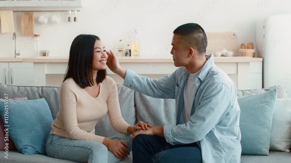 A young couple shares a sweet, intimate moment in a bright living room. They smile at each other while holding hands, enjoying each other's company in a casual, relaxed setting. A young couple shares a sweet, intimate moment in a bright living room. They smile at each other while holding hands, enjoying each other's company in a casual, relaxed setting.