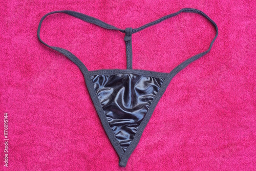 one female black thong latex panties lying on red cloth on table in room