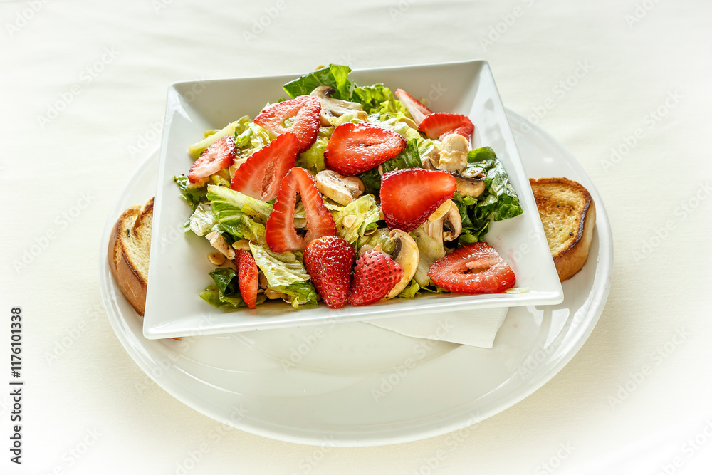 A salad with strawberries, lettuce, and mushrooms on a white plate A salad with strawberries, lettuce, and mushrooms on a white plate