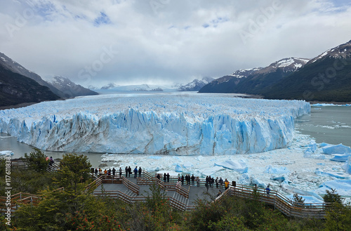 Stunning View of Perito Moreno Glacier with Visitors Observing the Towering Blue Ice Walls and Majestic Andes Mountains in the Distance: A Must-Visit Destination in the Heart of Patagonia, Argentina photo