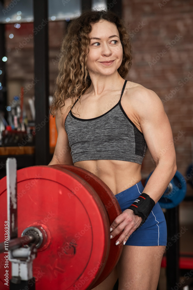 Fototapeta premium Caucasian forty year old woman putting a weight plate on a barbell in the gym. Vertical photo. 