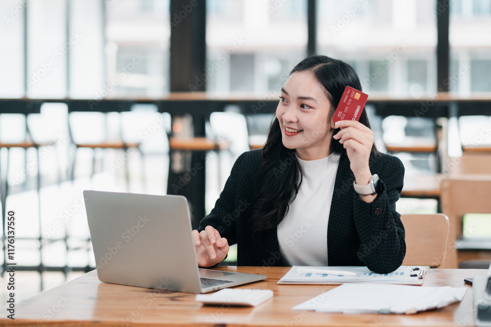 Smiling woman using a laptop and holding a credit card, representing online shopping or e-commerce in a modern office environment. Smiling woman using a laptop and holding a credit card, representing online shopping or e-commerce in a modern office environment.