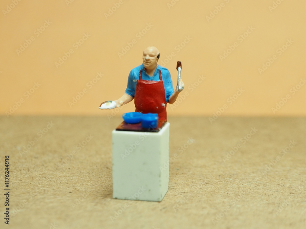 Naklejka premium Mini toy of action figure at with blurred background. Miniature photography concept design. Minifigure of chef character cooking at kitchen.