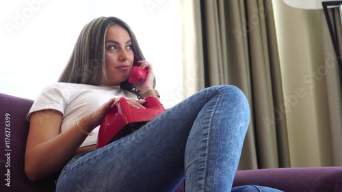 Young Beautiful Woman Talking Over Landline Rotary Telephone, Holding in Lap and Sitting on Couch photo