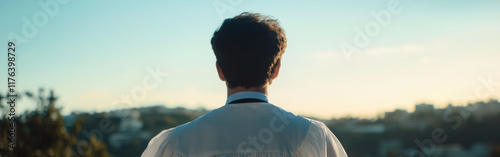 man in white shirt gazes into horizon, reflecting on his future. serene landscape and warm light create hopeful atmosphere