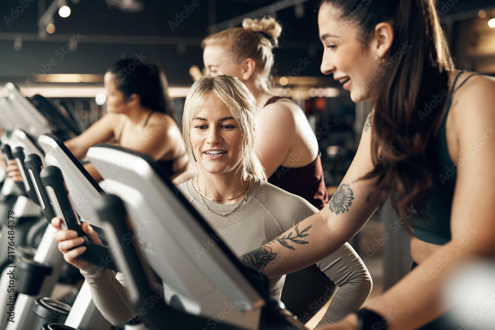 Smiling female instructor offering encouragement to a fit young woman riding a stationary bike during a cardio workout class in a gym Smiling female instructor offering encouragement to a fit young woman riding a stationary bike during a cardio workout class in a gym