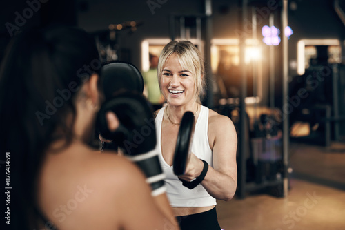 Smiling young woman in sportswear holding pads for a female partner practicing punching during a boxing workout session together in a gym photo