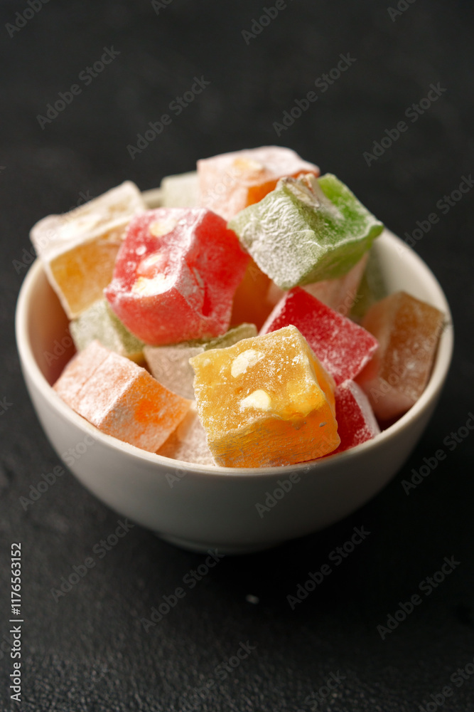 Colorful cubes of Turkish delight served in a white bowl on a dark surface for an enticing dessert display Colorful cubes of Turkish delight served in a white bowl on a dark surface for an enticing dessert display