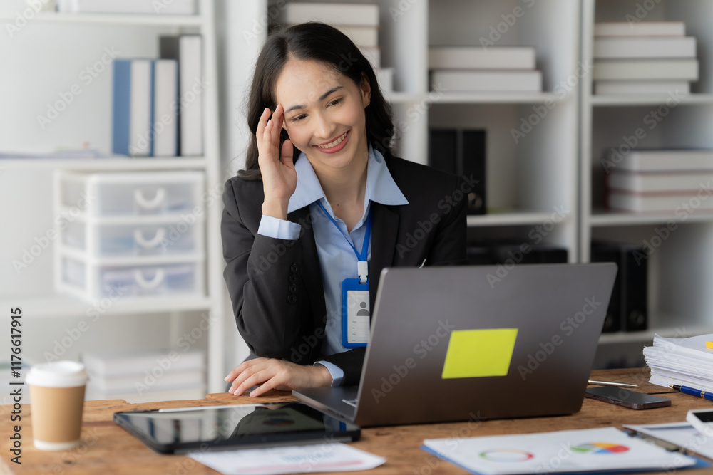 Confident Businesswoman Working on Laptop in Office: A smiling businesswoman with a name tag sits at her desk, focused on her laptop. The photo captures her professional confidence and success. Confident Businesswoman Working on Laptop in Office: A smiling businesswoman with a name tag sits at her desk, focused on her laptop. The photo captures her professional confidence and success.