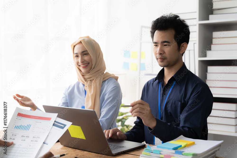 Focused Collaboration: A productive meeting of two diverse professionals, a man and a woman wearing a hijab, engaged in a serious discussion over a laptop and documents in a modern office setting. Focused Collaboration: A productive meeting of two diverse professionals, a man and a woman wearing a hijab, engaged in a serious discussion over a laptop and documents in a modern office setting.