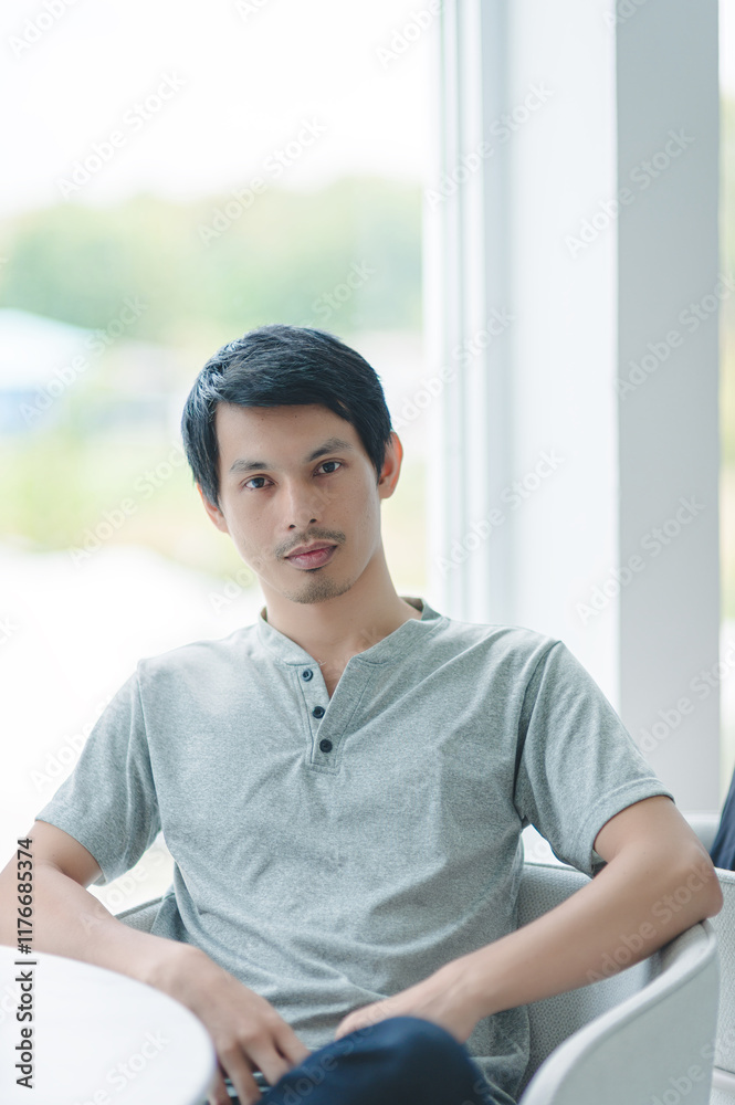 Young Man Sitting Near Window in Modern Indoor Setting Young Man Sitting Near Window in Modern Indoor Setting