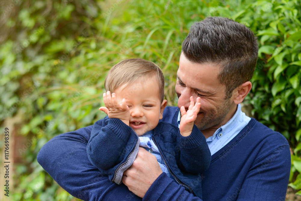 Caring father cuddling laughing infant wearing matching blue knitwear amid blooming garden, sharing warm sunlight and playful bonding moment Caring father cuddling laughing infant wearing matching blue knitwear amid blooming garden, sharing warm sunlight and playful bonding moment