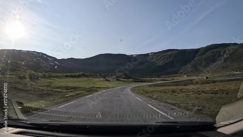 Driving along the E69 road in northern Norway's tundra. The barren landscape features moss, grass, and a few trees. The sea briefly appears on the right side, enhancing the remote beauty. photo