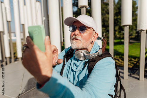 Smiling senior man wearing backpack and clicking pictures at park photo