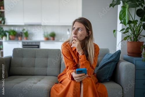 Canvas Print Thoughtful serious woman waits for message or call on phone, sitting alone on couch at home