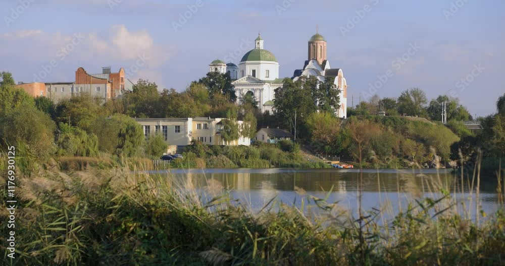 A peaceful riverside scene with lush greenery, a bridge, and historic buildings, including a church with a dome. The calm water reflects the serene atmosphere of the sunny day. A peaceful riverside scene with lush greenery, a bridge, and historic buildings, including a church with a dome. The calm water reflects the serene atmosphere of the sunny day.